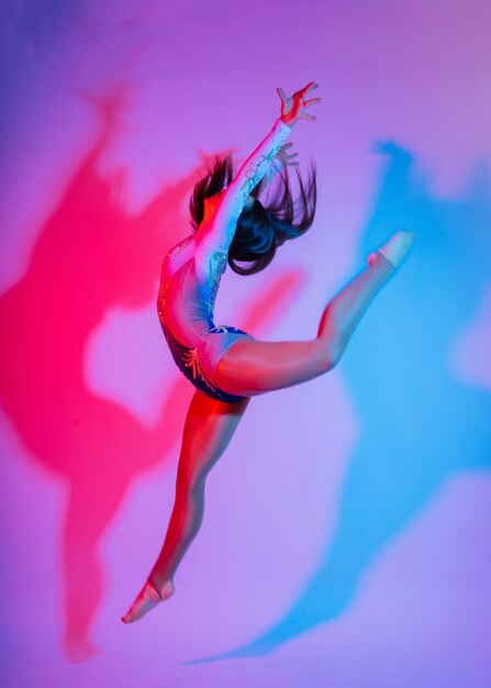 A girl gymnast in a swimsuit does tricks on a white and dark background front view