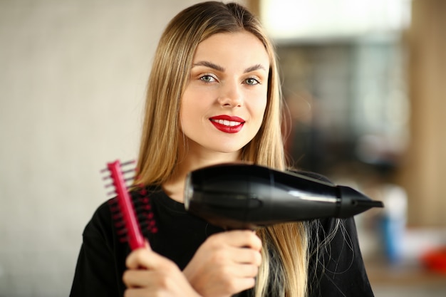 Girl hairdresser crossed hands with comb and dryer. beautiful hairstylist holding hairbrush and hairdryer for styling haircut.