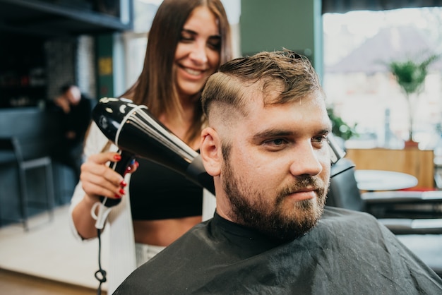 Photo girl hairdresser dries hair to a man in a salon