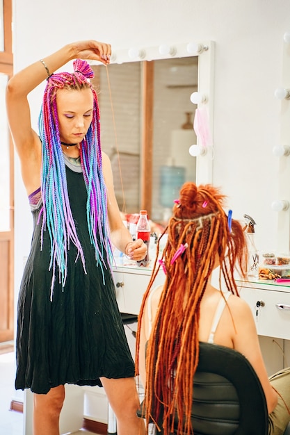 Girl hairdresser with colored afro braids weaves to female ginger dreadlocks weaving process with ka...