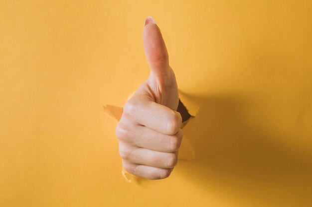 Photo girl hand breaks the yellow paper and shows a gesture