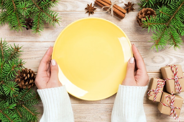 Girl hand hold Empty yellow plate with christmas decoration. New Year concept Top view
