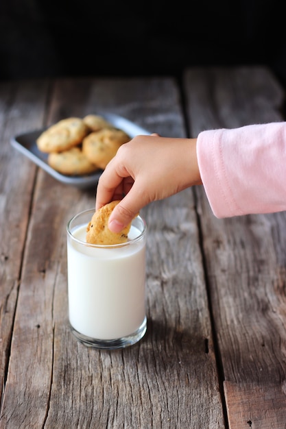 女の子手ピッキングバタークッキーは牛乳に浸します。甘いデザートと健康的な飲み物。