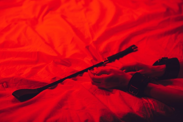 Girl hands in handcuffs and leather whip flogger for BDSM sex with submission and domination lie on bed