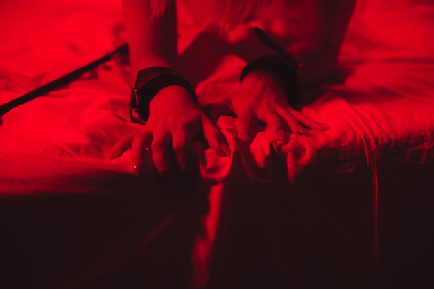 Photo girl hands in handcuffs and leather whip flogger for bdsm sex with submission and domination lie on bed