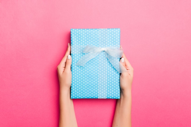 Girl Hands holding craft paper gift box with as a present for Christmas or other holiday on pink background