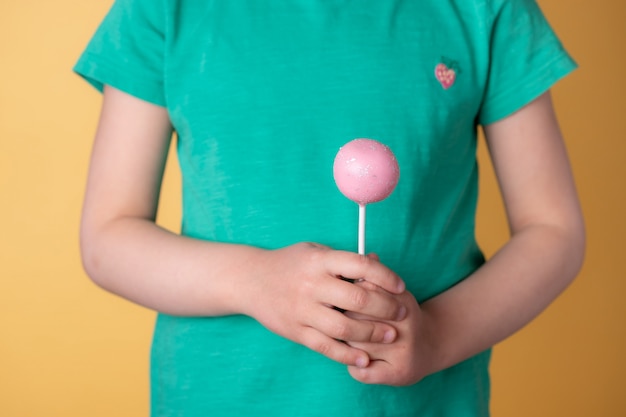 Girl hands holding tasty pink cake pops, candy on a stick. yellow wall