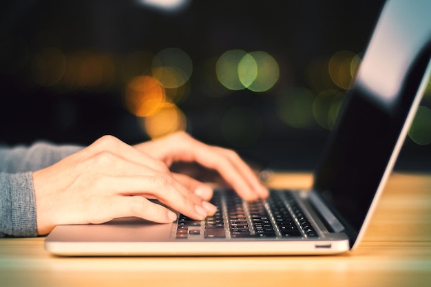 Girl hands typing on laptop on wooden table at night close up