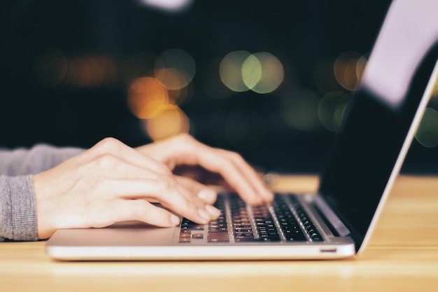 Girl hands typing on laptop on wooden table at night