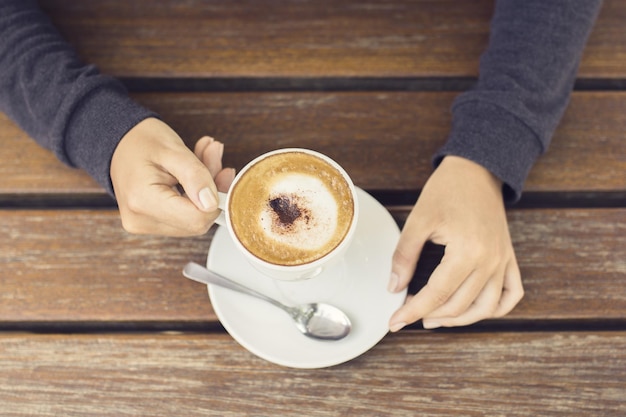 木製のテーブルの上のコーヒー カップを持つ少女の手