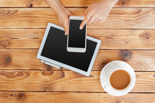 Girl hands with digital tablet and cup of coffee on a wooden table