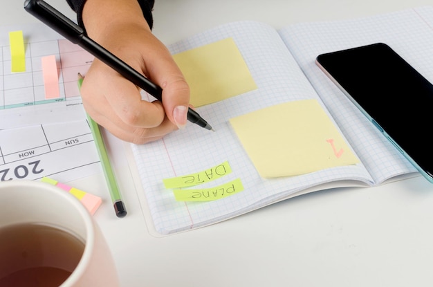 Photo girl hands with mobile phone with calendar writing and list of work in diary on desk