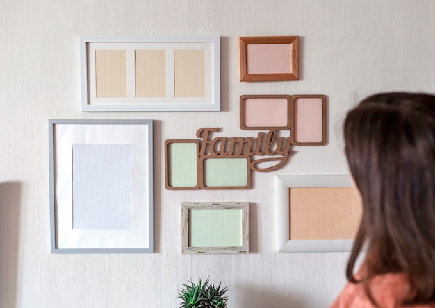 Photo girl hanging frame on white wall with set of different empty vertical and horizontal picture frames to create family photo gallery, to capture a moment, mockup template on white wall, lifestyle