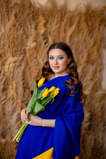 The girl has a dress from the flag of Ukraine as a symbol of the country and holds yellow tulips