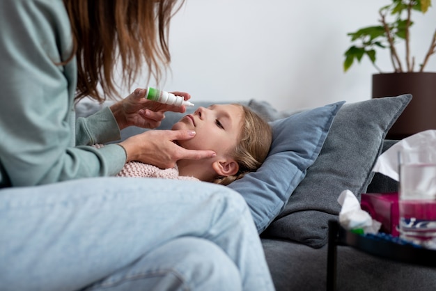 Girl has a runny nose and her mother sprays medicine into her nose