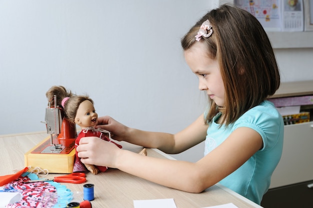 The girl has sewn a new dress and dressed it on a doll.