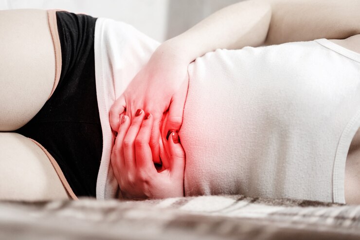 소녀는 복통이 있고 소녀는 침대에 누워 있고 복부에 빨간 악센트가 있습니다.