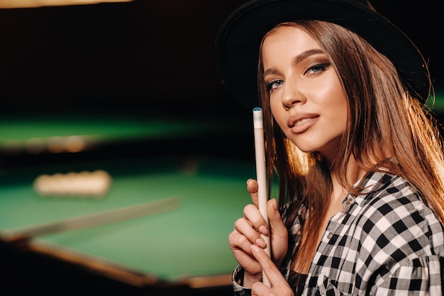 A girl in a hat in a billiard club with a cue in her hands.billiards Game.