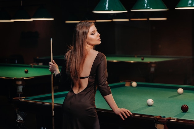 A girl in a hat in a billiard club with a cue in her hands.Pool Game.