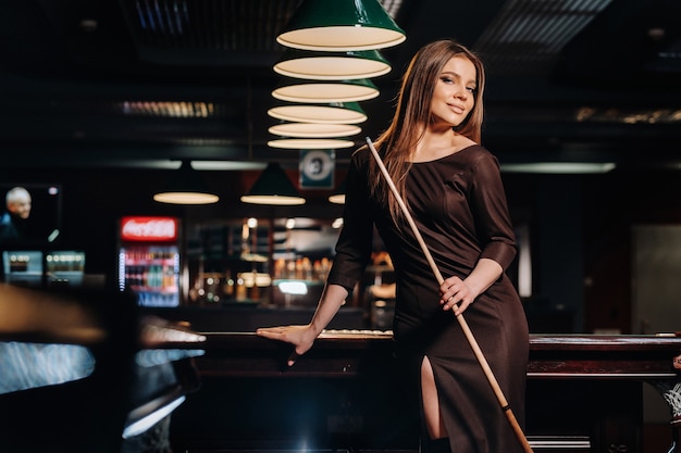 A girl in a hat in a billiard club with a cue in her hands