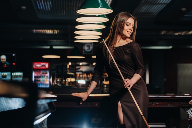 A girl in a hat in a billiard club with a cue in her hands