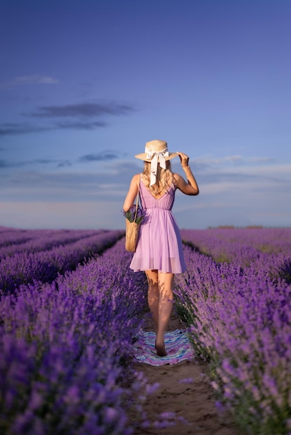 Photo girl in a hat and a lilac dress runs into a field of lavender view from the back