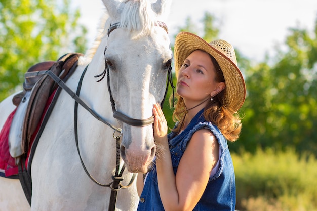 The girl in a hat looks at a horse and irons it on a muzzle