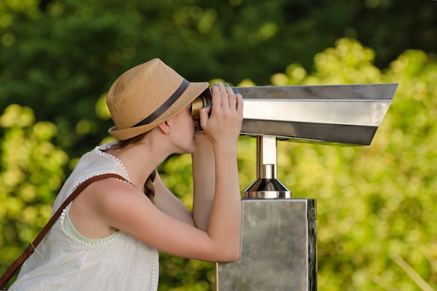 Girl in hat looks into big binoculars