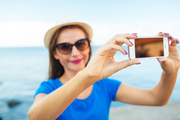 Girl in the hat making selfie by the smartphone on the background of sea coast adriatic sea