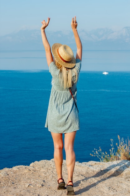 A girl in a hat near the sea on the edge of a cliff.