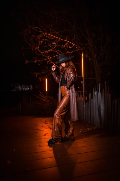 Girl in a hat in a portrait at night on a parcel. Brunette Caucasian model looking at camera, illuminated with orange light