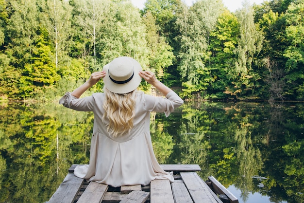 Girl in a hat resting on the autumn lake on the bridge