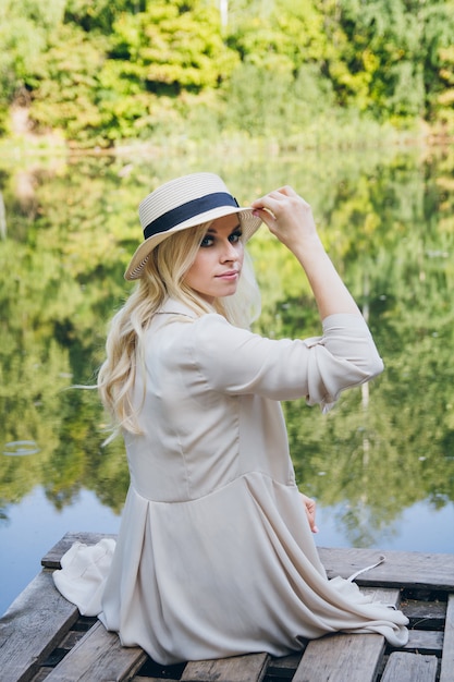 Girl in a hat resting on the autumn lake on the bridge