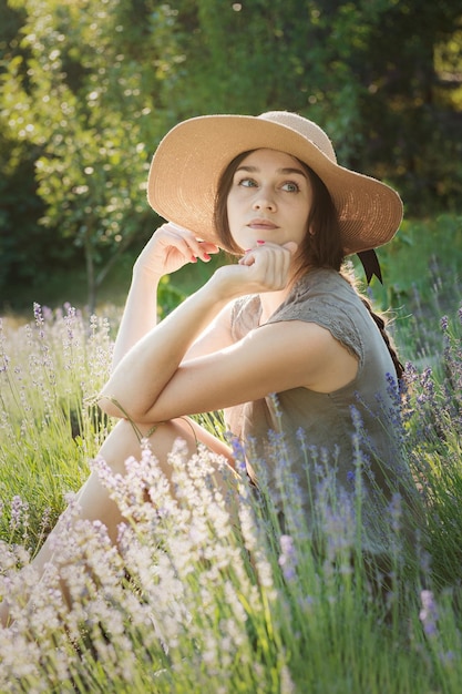 The girl in the hat sit in the middle of a lavender field