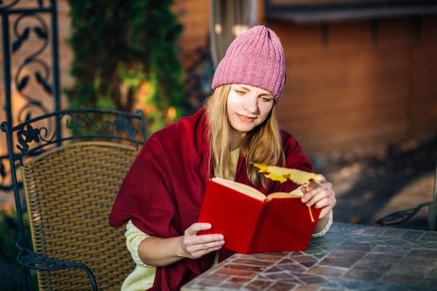 帽子とセーターを着た女の子がカフェのテーブルに座って本を読む