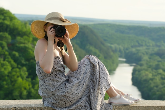 Girl in hat takes pictures near forest and river