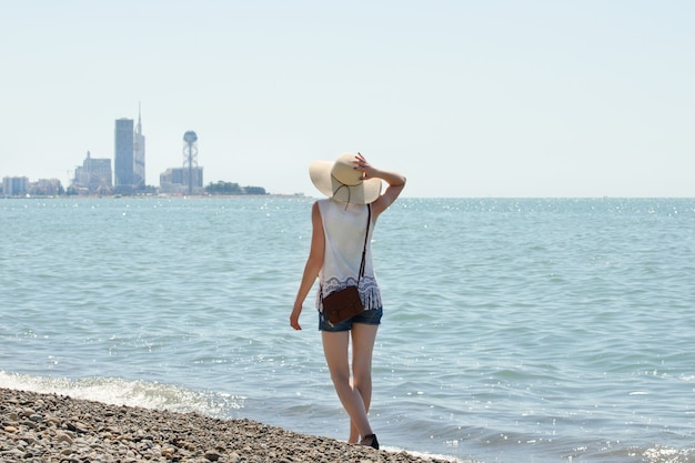 Girl in a hat walks along the seashore