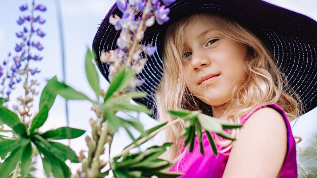 The girl in the hat walks in a field of lupines.