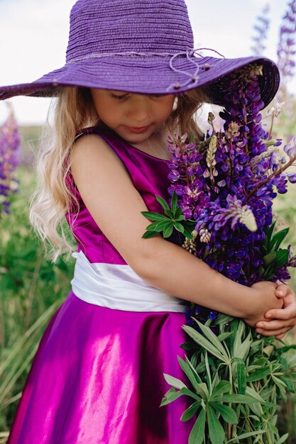 The girl in the hat walks in a field of lupines.