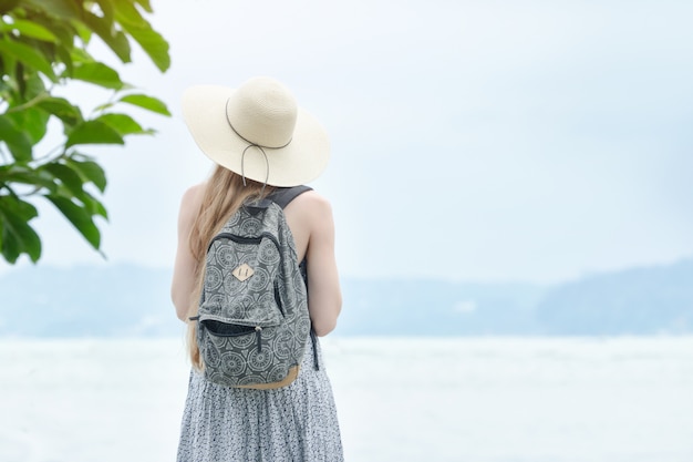 Girl in a hat with a backpack standing on a pier at the sea.