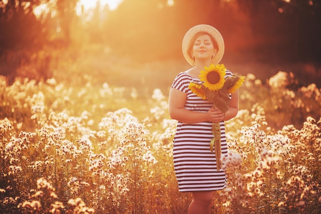 The girl in a hat with a bouquet of sunflowers poses