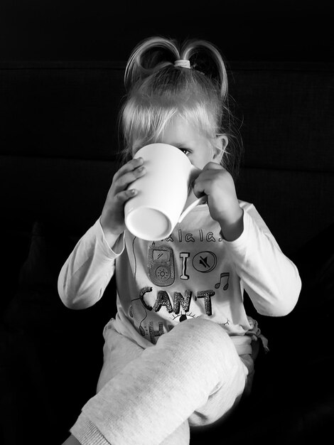 Photo girl having drink while sitting against black background