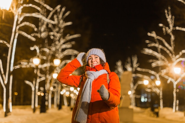 Girl having fun on christmas decoration lights street. Young happy smiling woman wearing stylish knitted scarf and jacket outdoors. Model laughing. Winter wonderland city scene, New Year party.