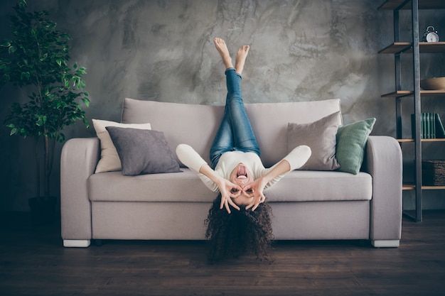 girl having fun lying sofa showing ok-sign like glasses in modern loft industrial style interior