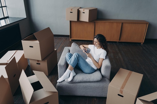 Girl having rest in new apartment and clicks phone Independent spanish woman is moving