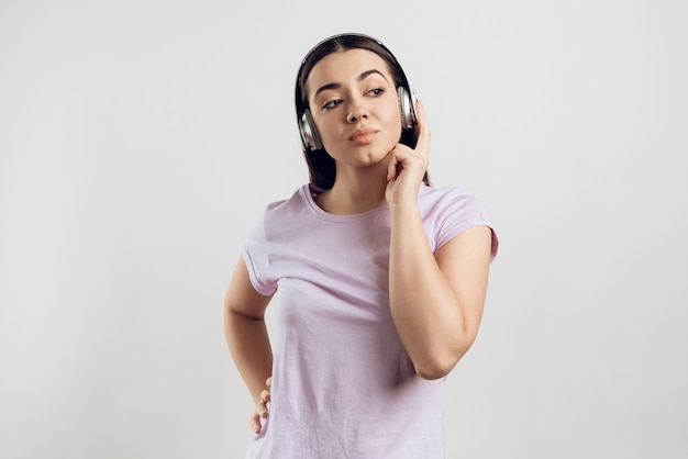 Girl in headphones listens to classical in white room.