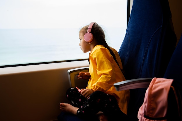 A girl in headphones on a train looks out the window. Journey.