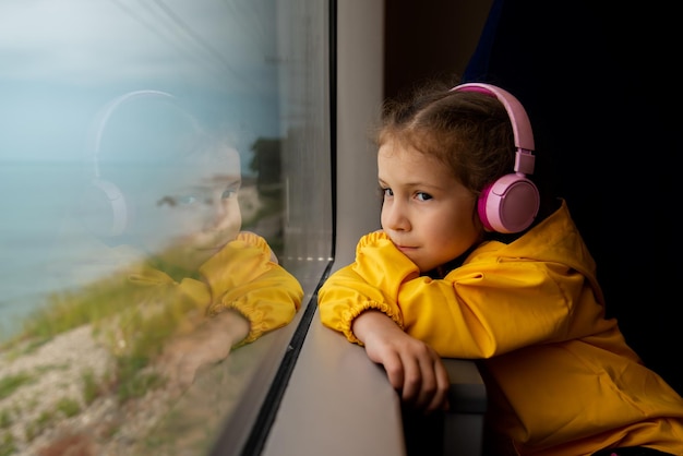 Девушка в наушниках в поезде смотрит в окно Путешествие