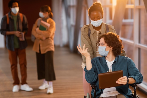 Girl helping her colleague in wheelchair go to class