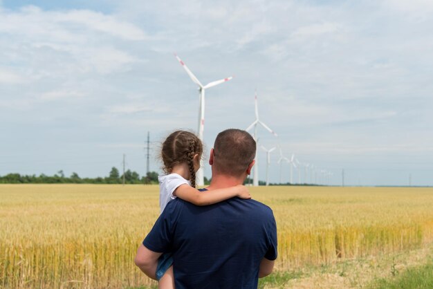 한 소녀와 그녀의 아빠가 들판에서 풍력 발전기를 바라보는 생태 미래